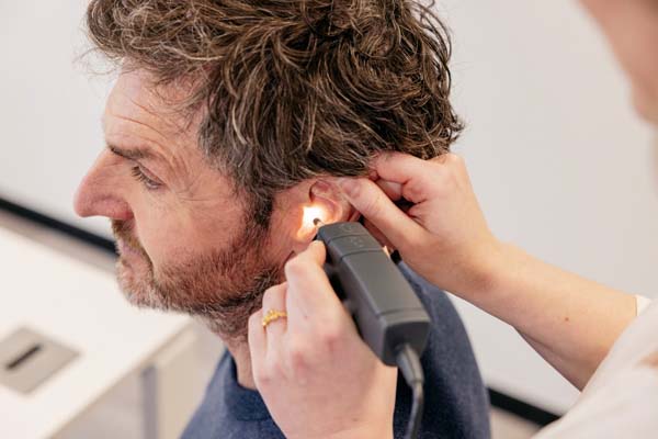Dokter schijnt met speciale lamp op klant zijn oor